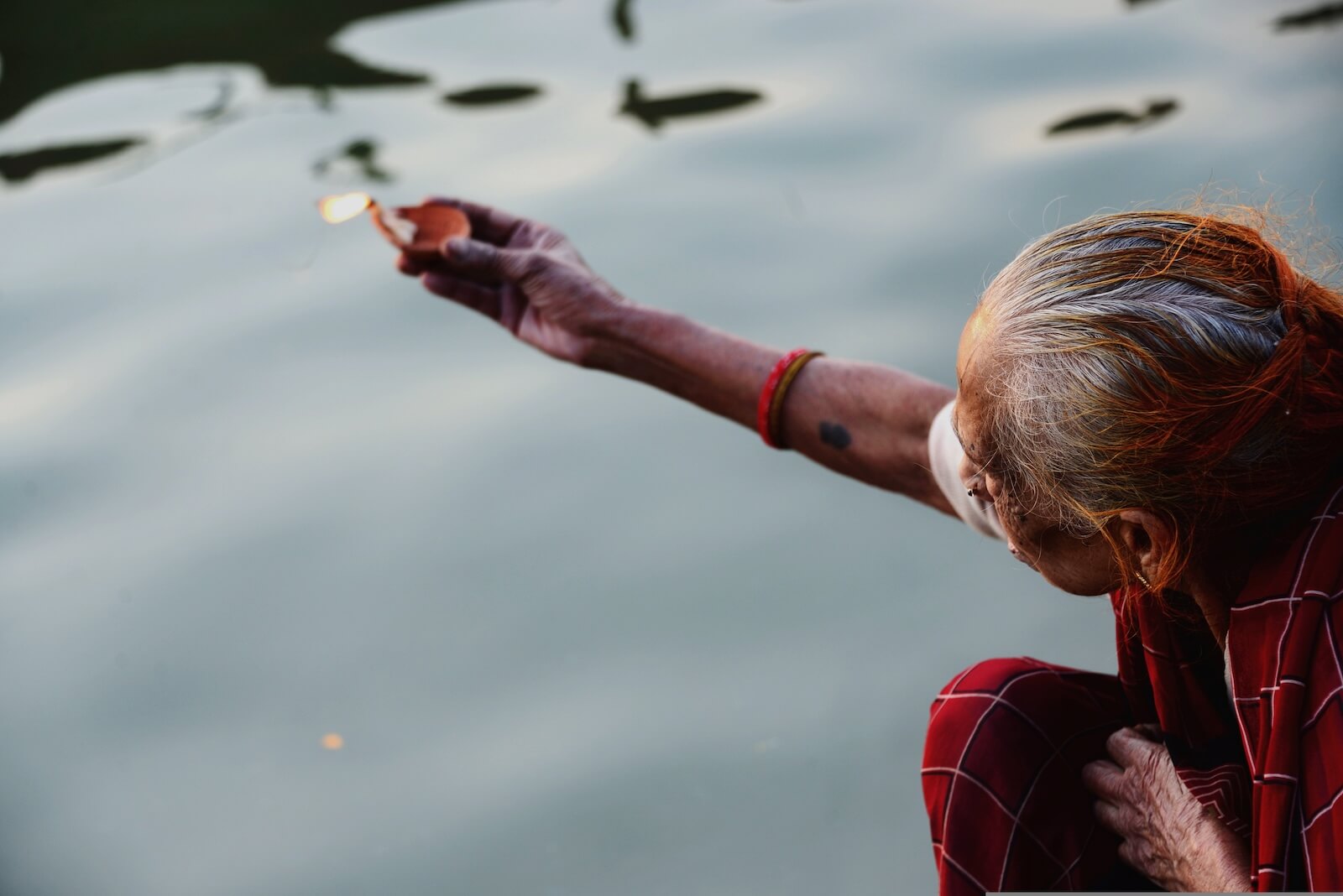 An old lady holding a diya in her hand over the Ganges