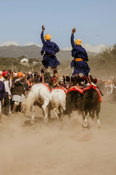 Two men standing on horses during the Hola Mohalla festival in Punjab, India