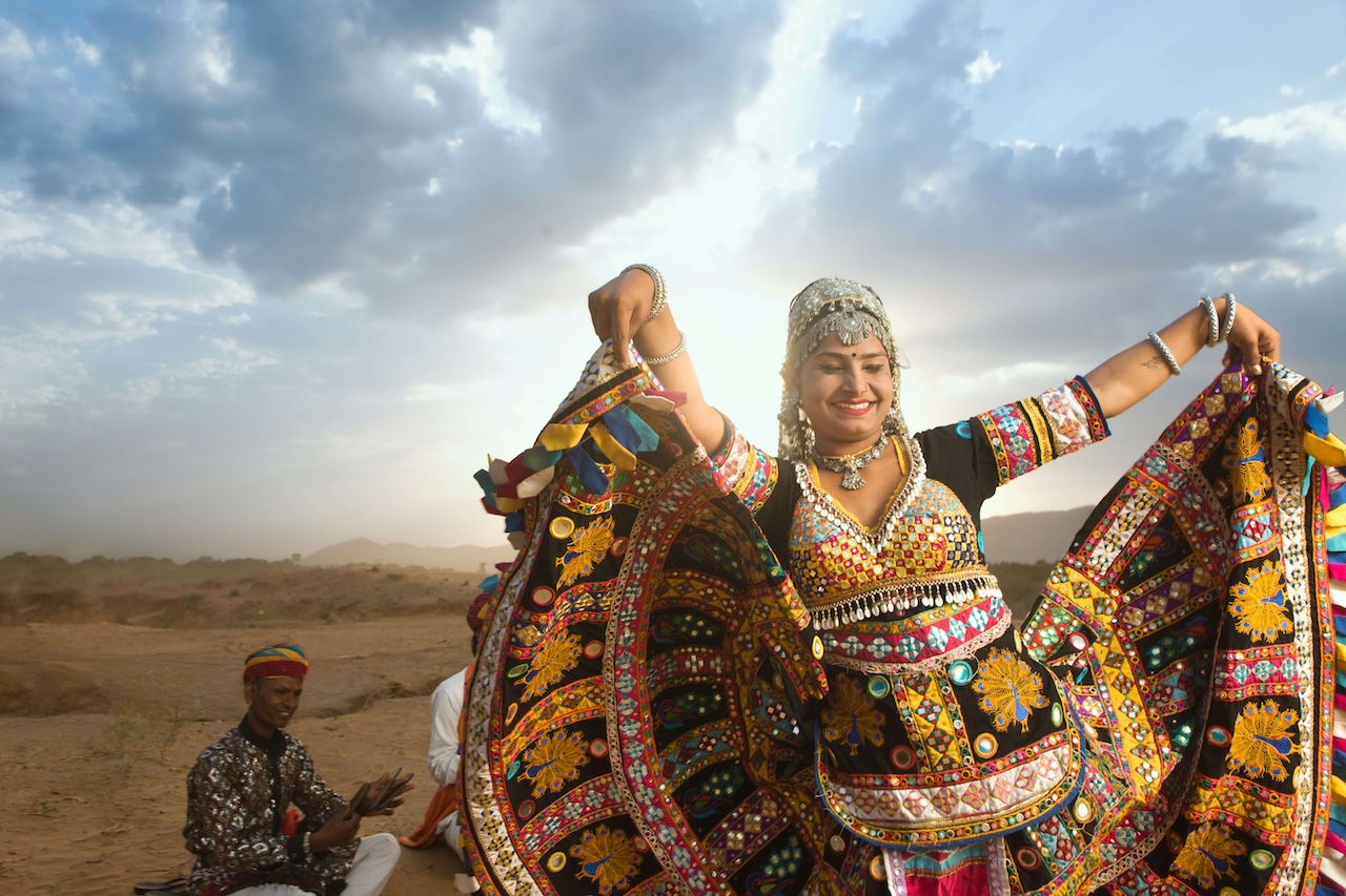 A woman in traditional Rajasthani attire dancing gracefully in richly embroidered and mirrored ghagra choli.